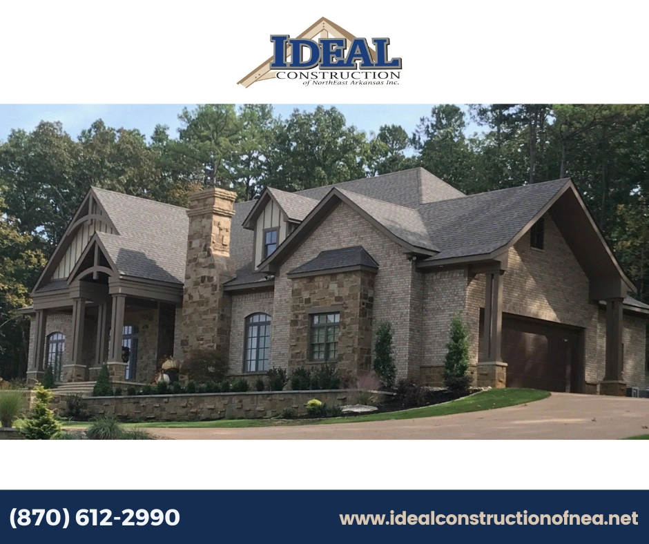 A large, newly constructed stone and brick home with a dark gray roof, surrounded by trees and landscaping.